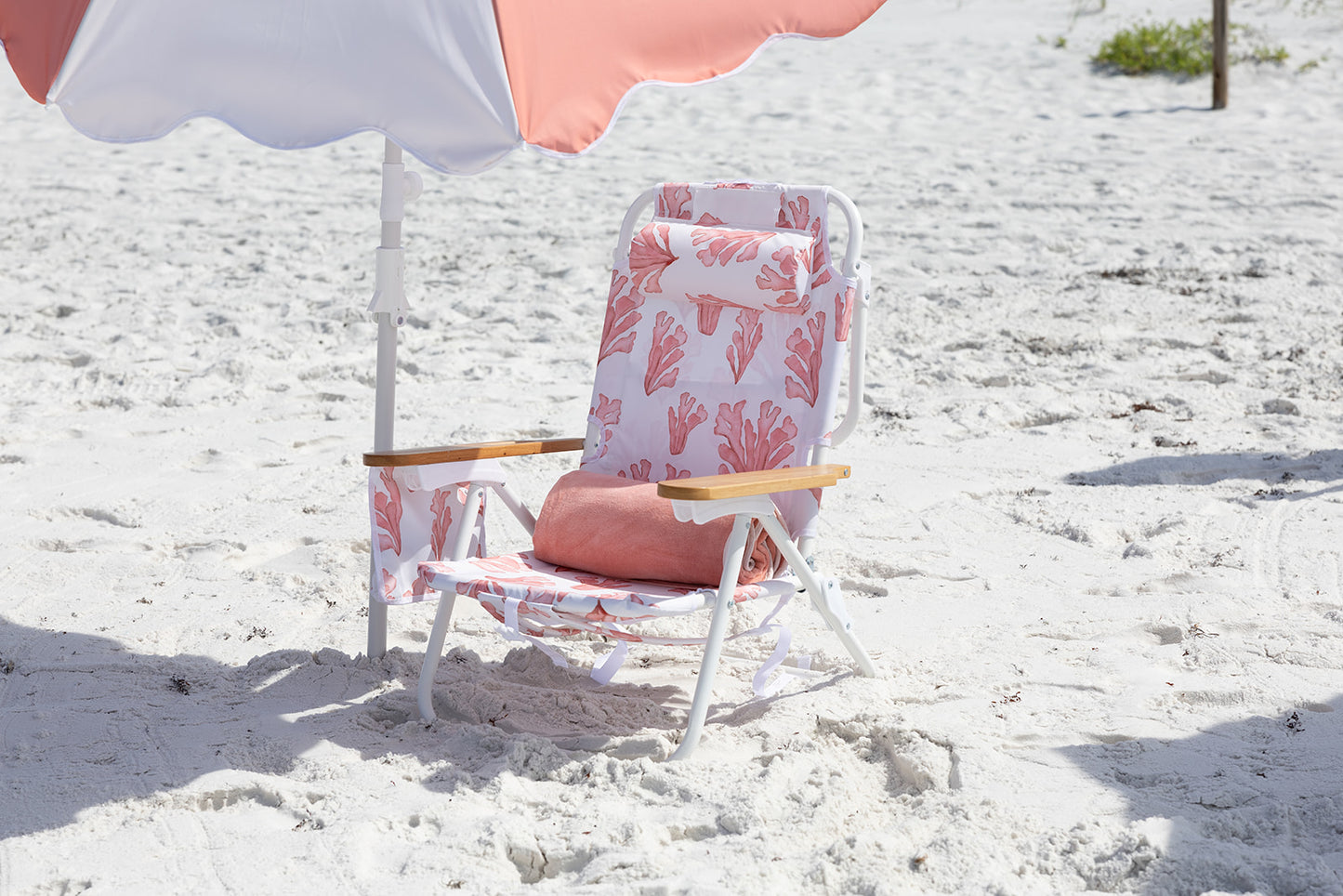 Beach chair with coral floral pattern and coral umbrella on a pristine fine sand beach
