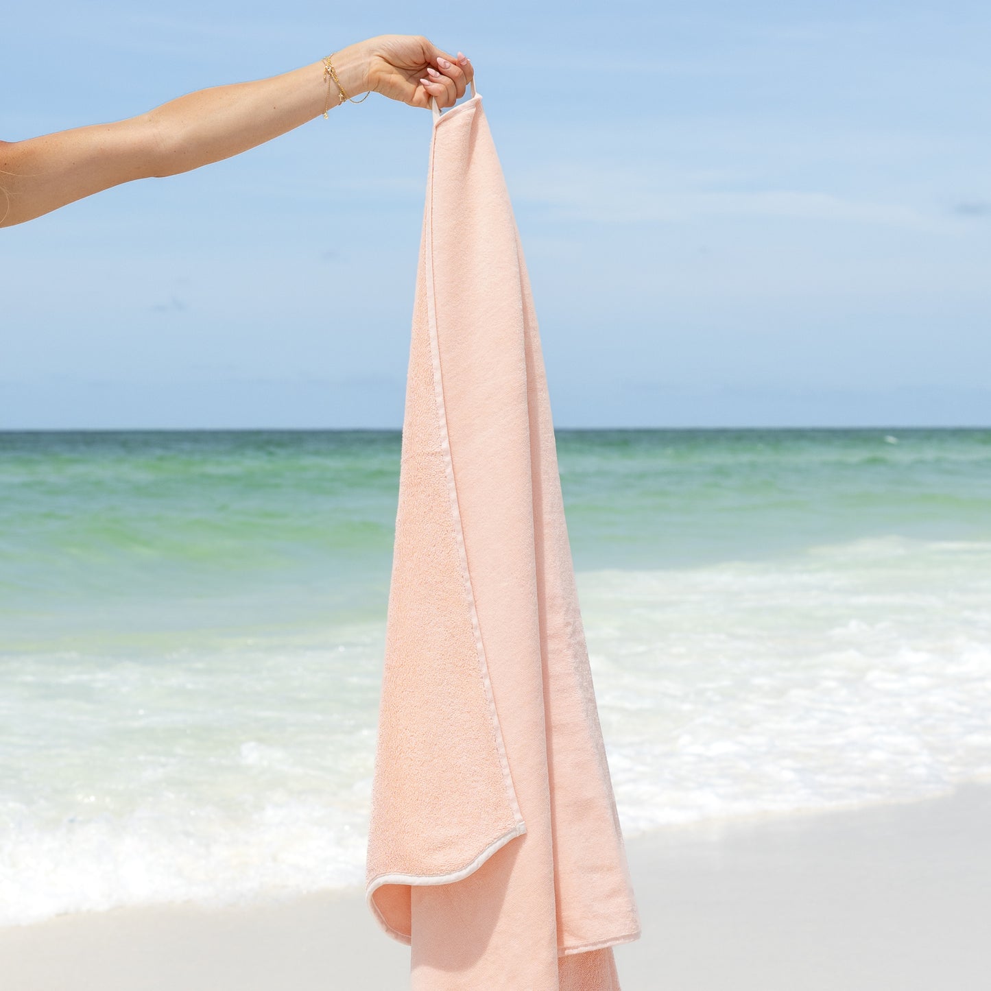 Woman holding a pink-colored towel with a beach and gulf background