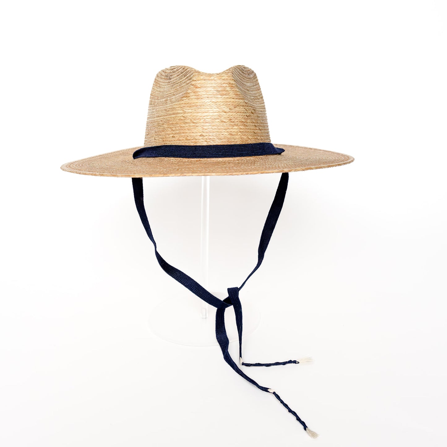 A beige rancher palm hat with a navy blue removable band and a cedar ball fastener.