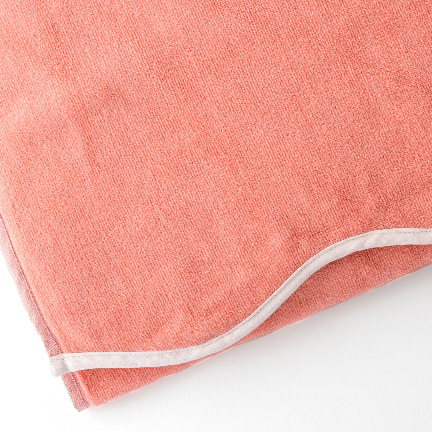Close-up of a coral-colored beach towel with a scalloped edge.