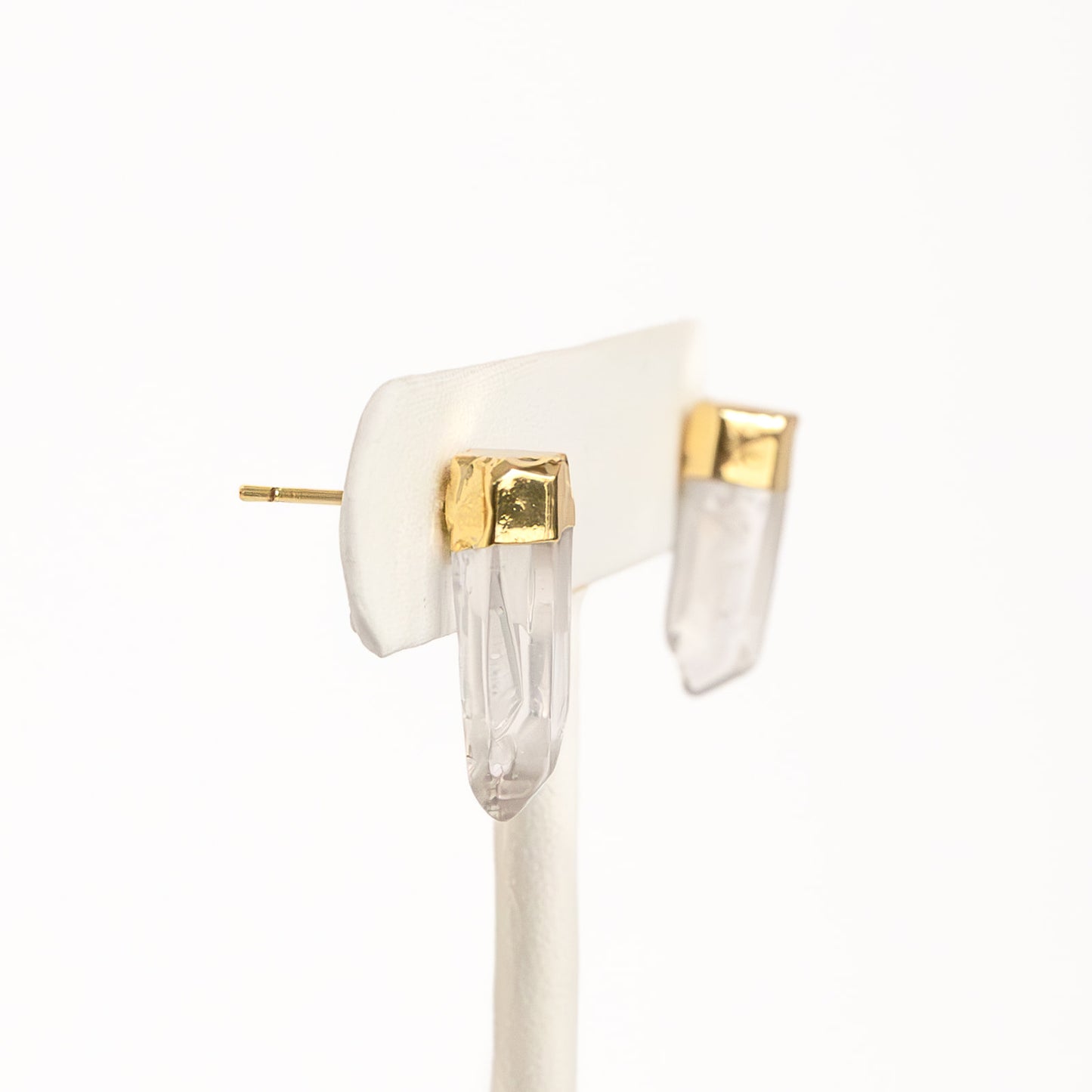 A pair of gold-colored pierce earrings on a white display stand.