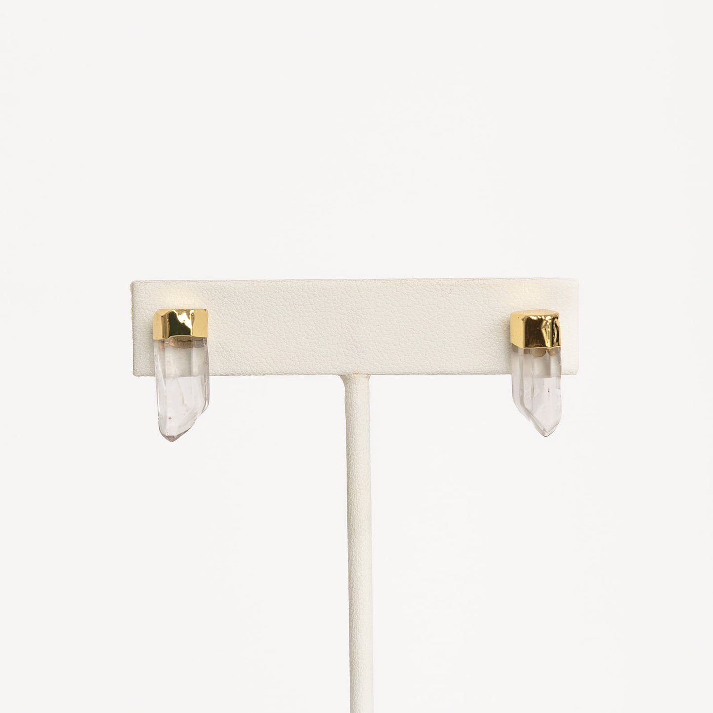 A pair of gold-colored pierce earrings on white stand