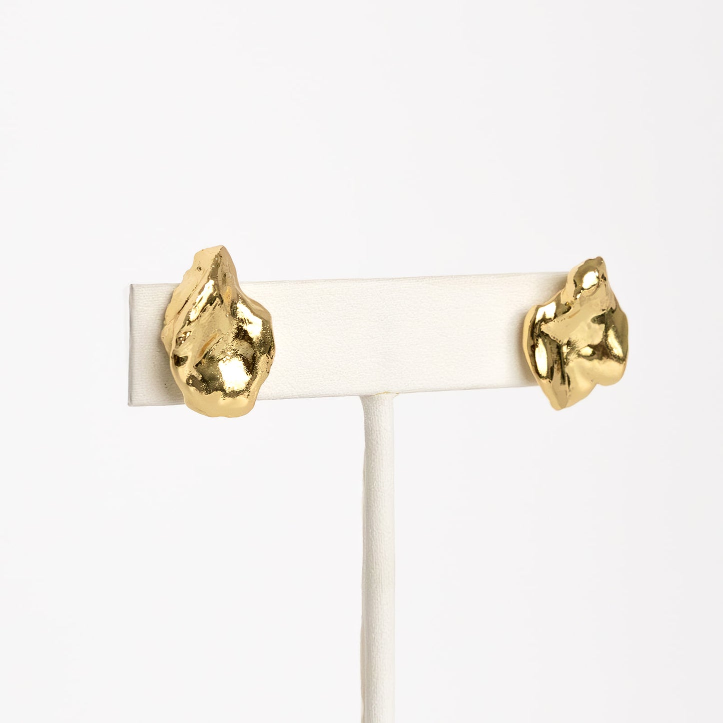 A pair of gold-colored earring studs on a white display stand, showcasing their dipped design.
