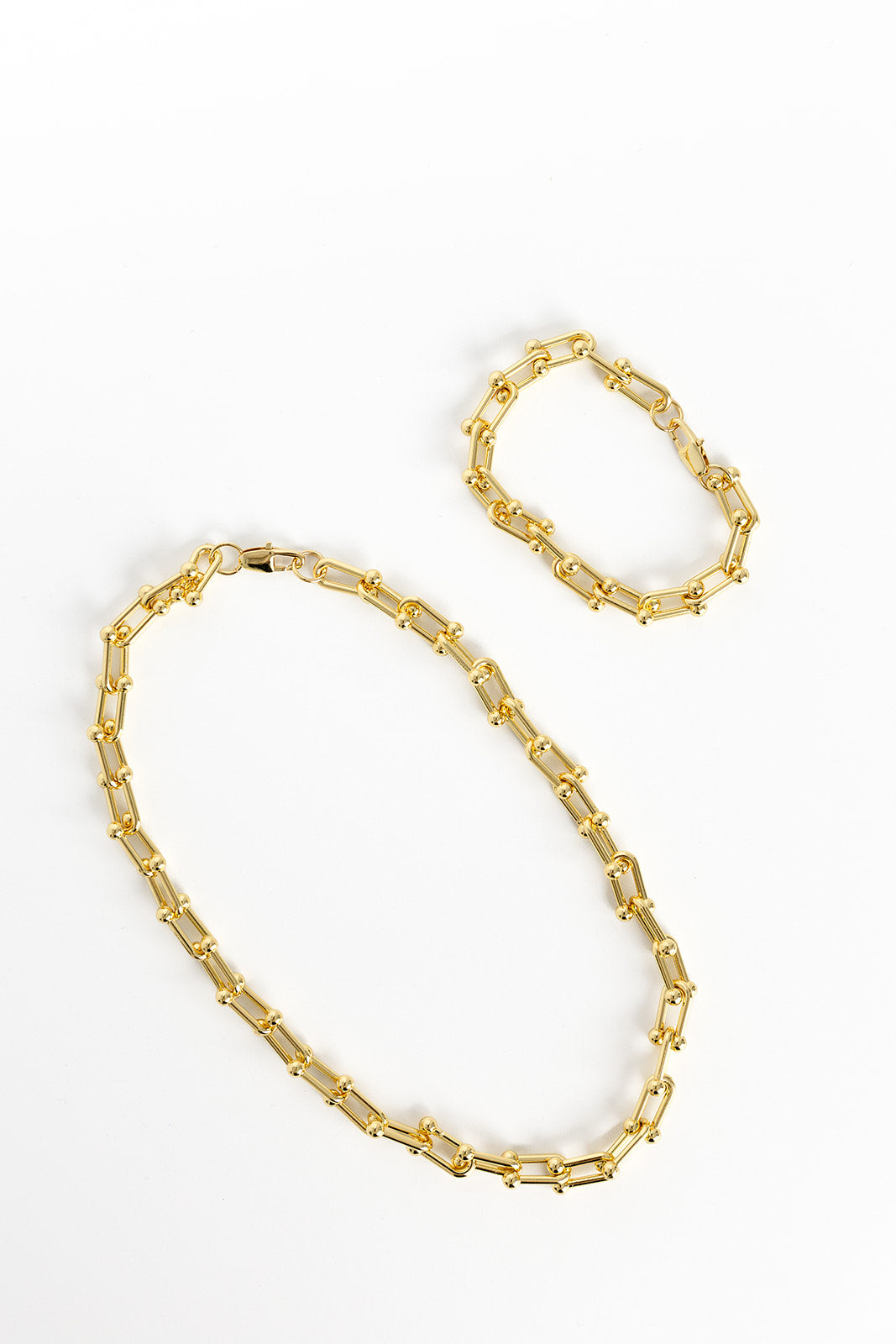 Gold horseshoe necklace laying next to gold horseshoe bracelet