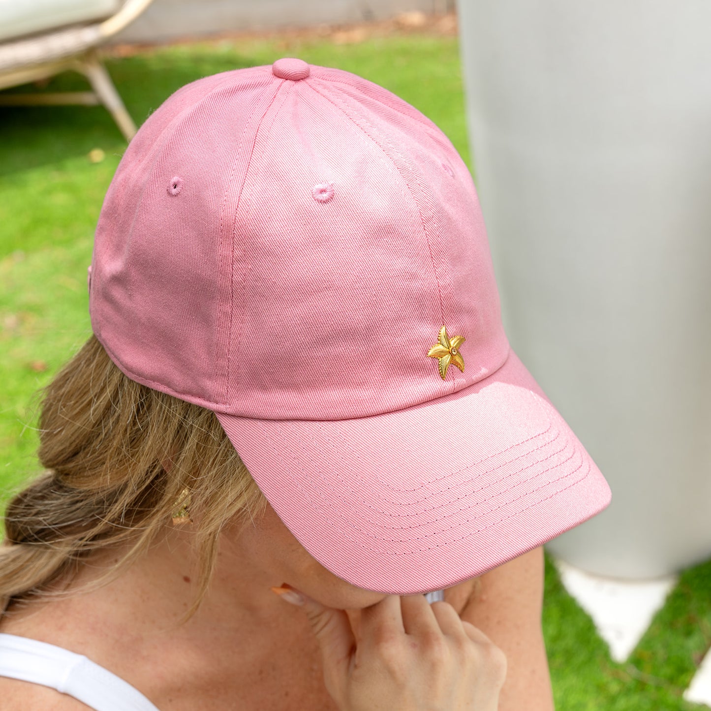 Blonde woman wearing a pink hat with a golden starfish design.