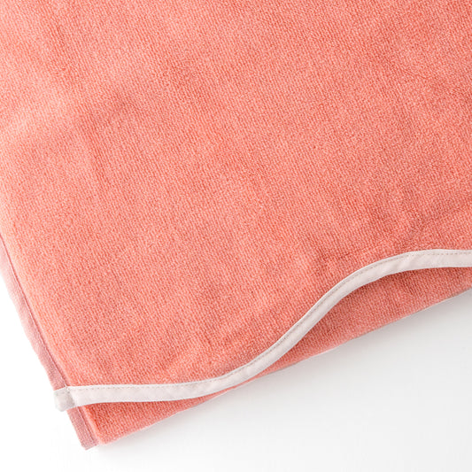 Close-up of a coral-colored beach towel with a scalloped edge.