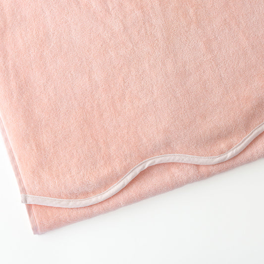 Close-up of a pink colored scalloped edge beach towel with a white border.