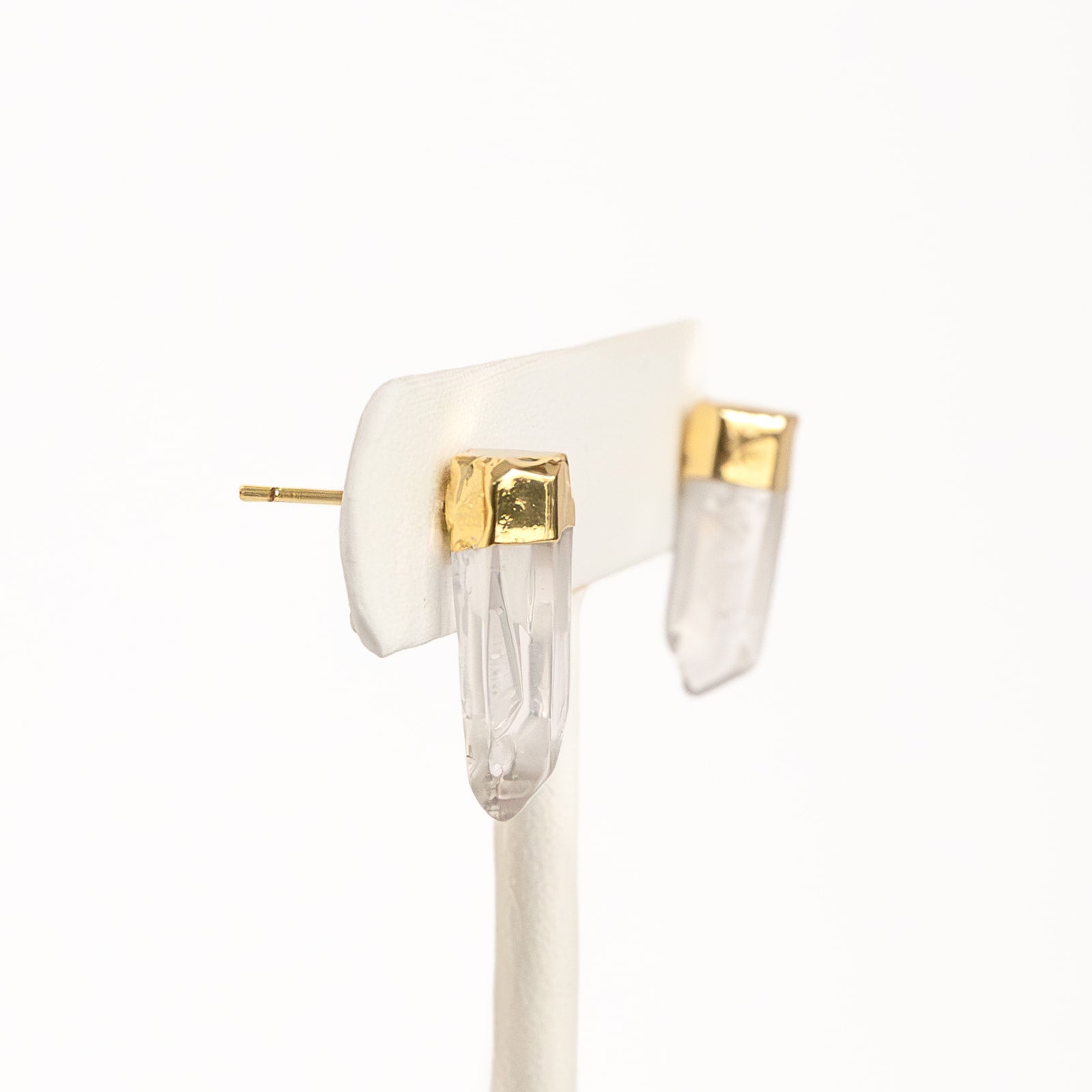 A pair of gold-colored pierce earrings on a white display stand.