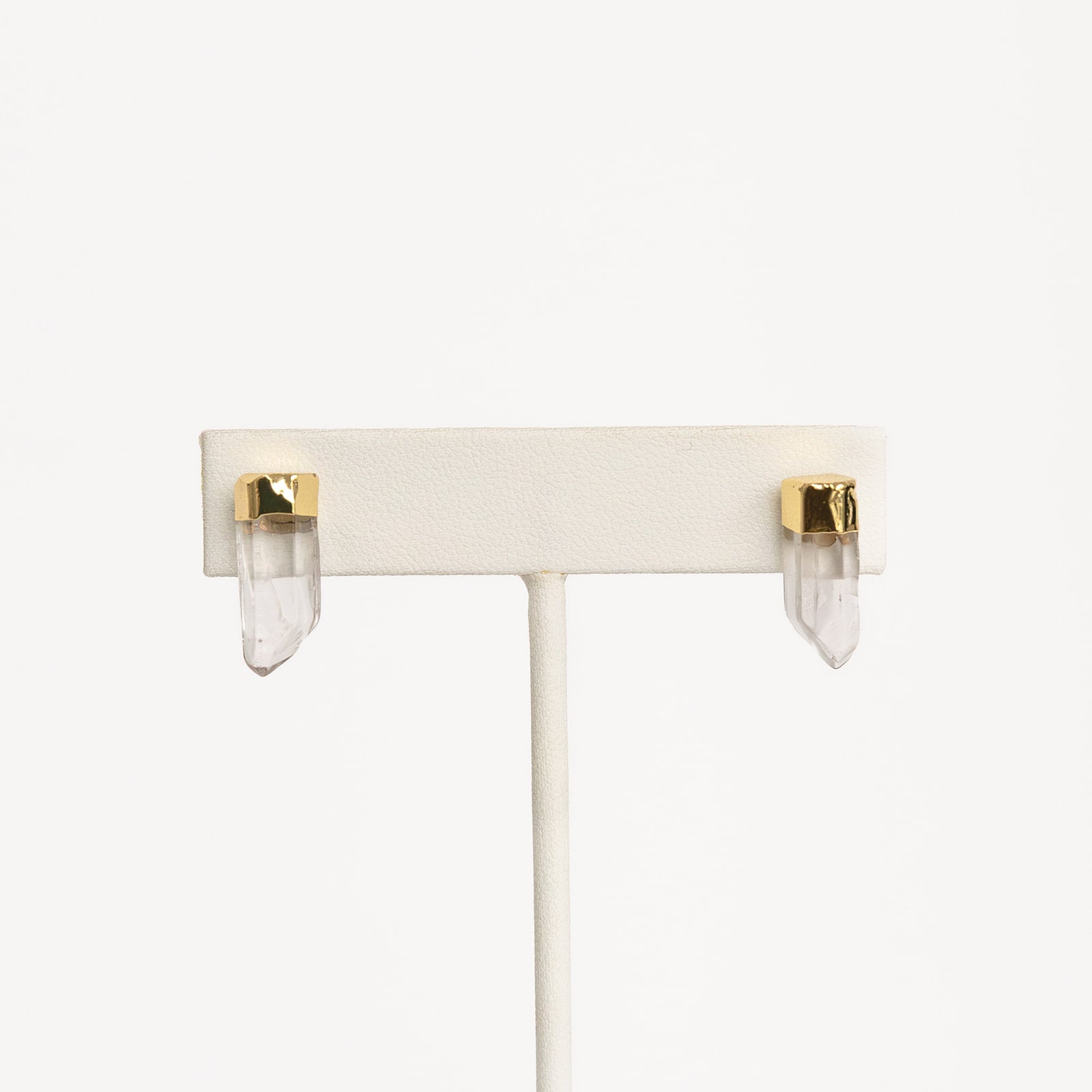 A pair of gold-colored pierce earrings on white stand