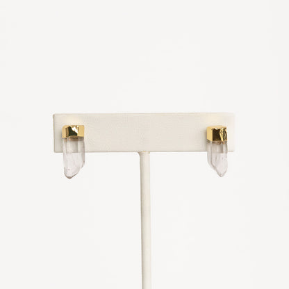 A pair of gold-colored pierce earrings on white stand
